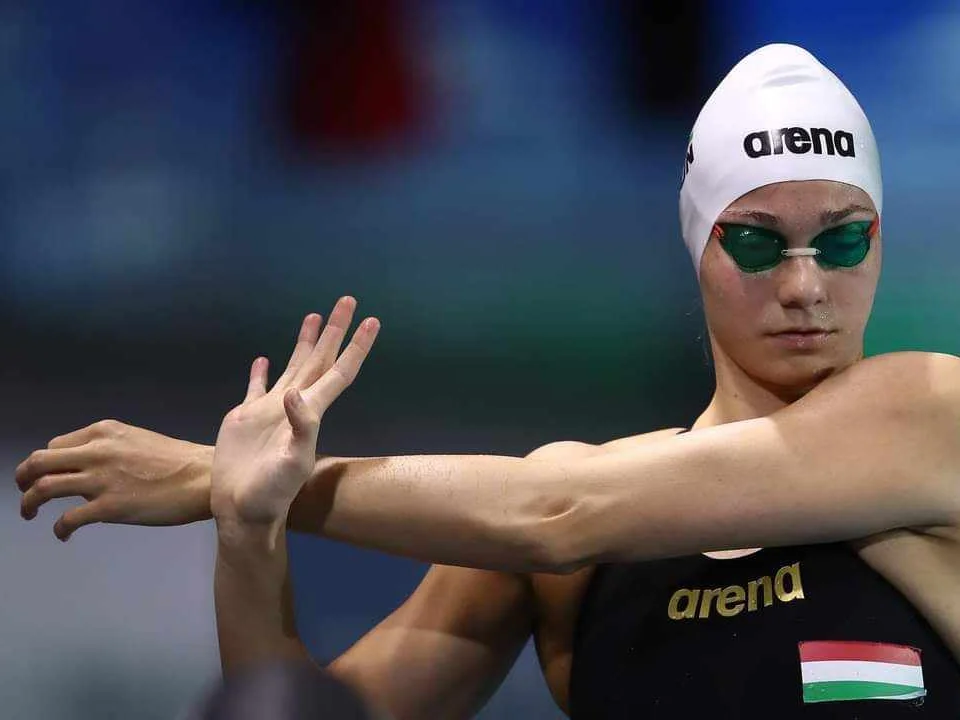 Reka Gyorgy, in a Hungary team suit and white cap, stretches her arms before a race